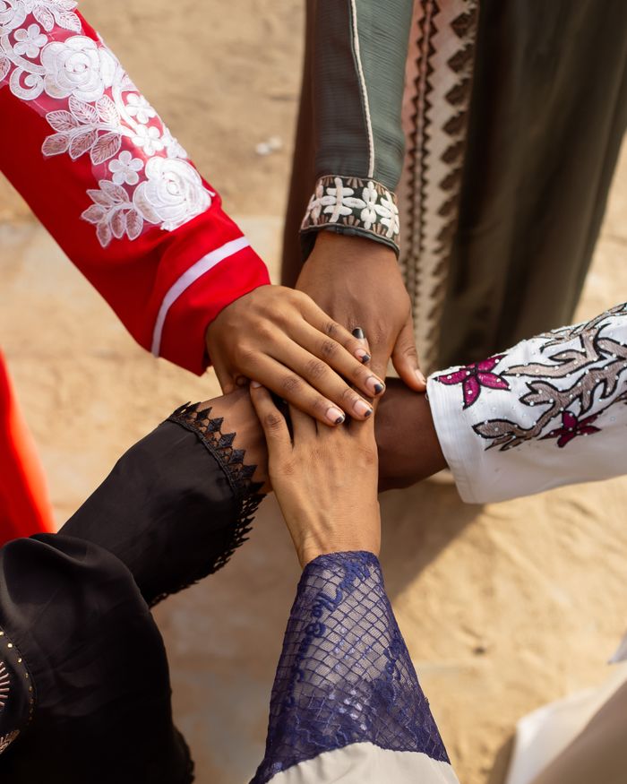 why-choose-us A group of people joining hands wearing colorful traditional attire outdoors, symbolizing unity.