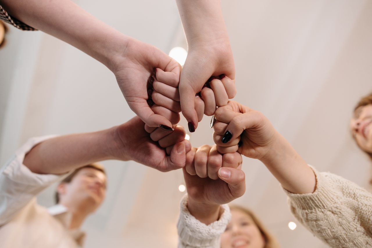 services-01 Close-up of a diverse group joining fists in a show of unity and teamwork indoors.