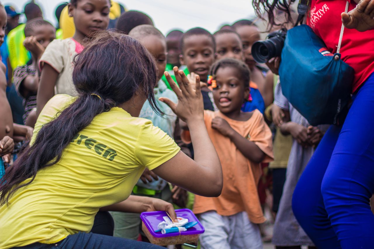 about-01 A woman engages with children through a high-five in a vibrant community setting.